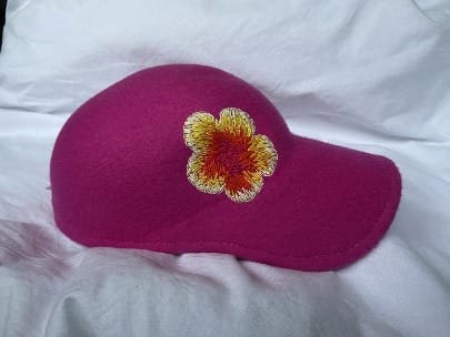 Fuchsia pet met een geborduurde bloem in geel, oranje en rood, op een witte doek