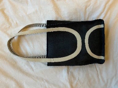 Zwarte leren tas met lichte gebogen biezen en twee hengsels, op een witte doek