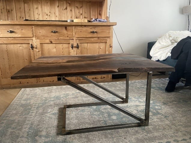Salontafel met een houten blad met zwarte epoxy op een schuin stalen onderstel, in een woonkamer