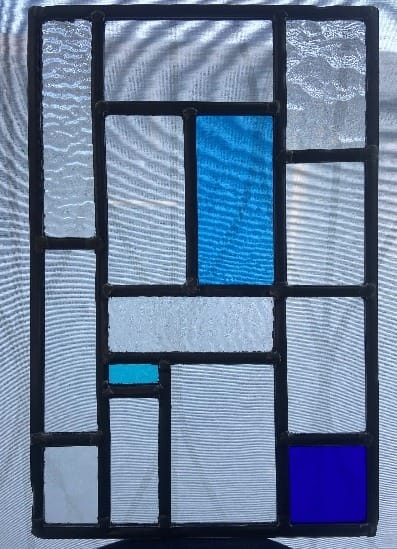 Glas-in-loodpaneel met rechthoeken in helder, blauw en structuurglas, tegen het licht
