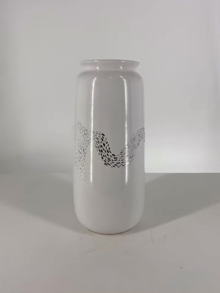 Hoge witte vaas met een band van kleine zwarte motieven, tegen een lichte achtergrond