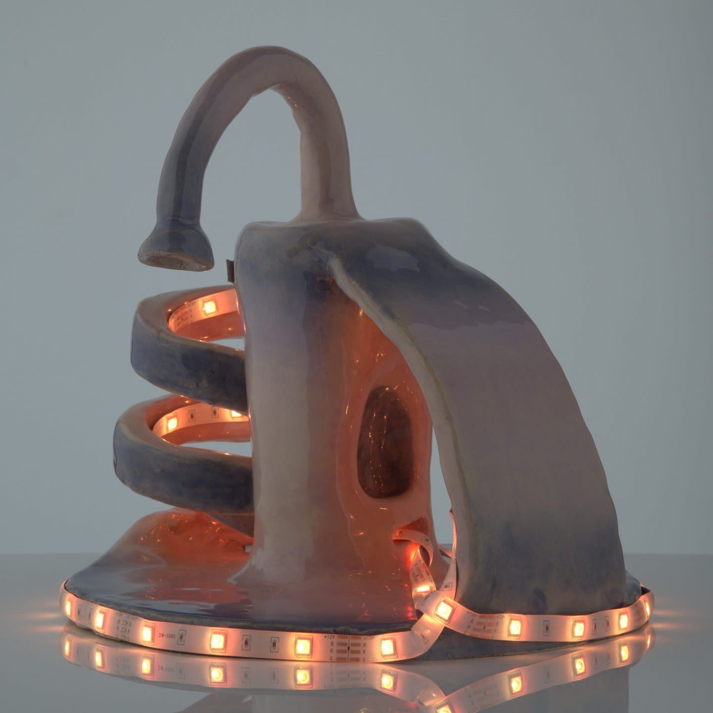 Lichtobject van klei met een spiraalvorm en een gebogen arm, verlicht door een oranje ledstrip