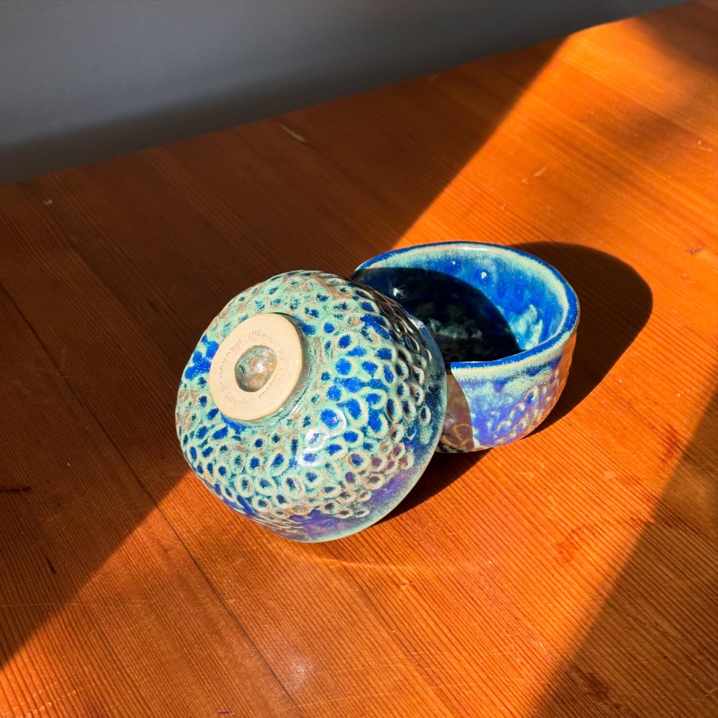 Twee blauwe kommetjes met een gehamerde textuur in fel zonlicht op een houten tafel, een ervan op zijn kop