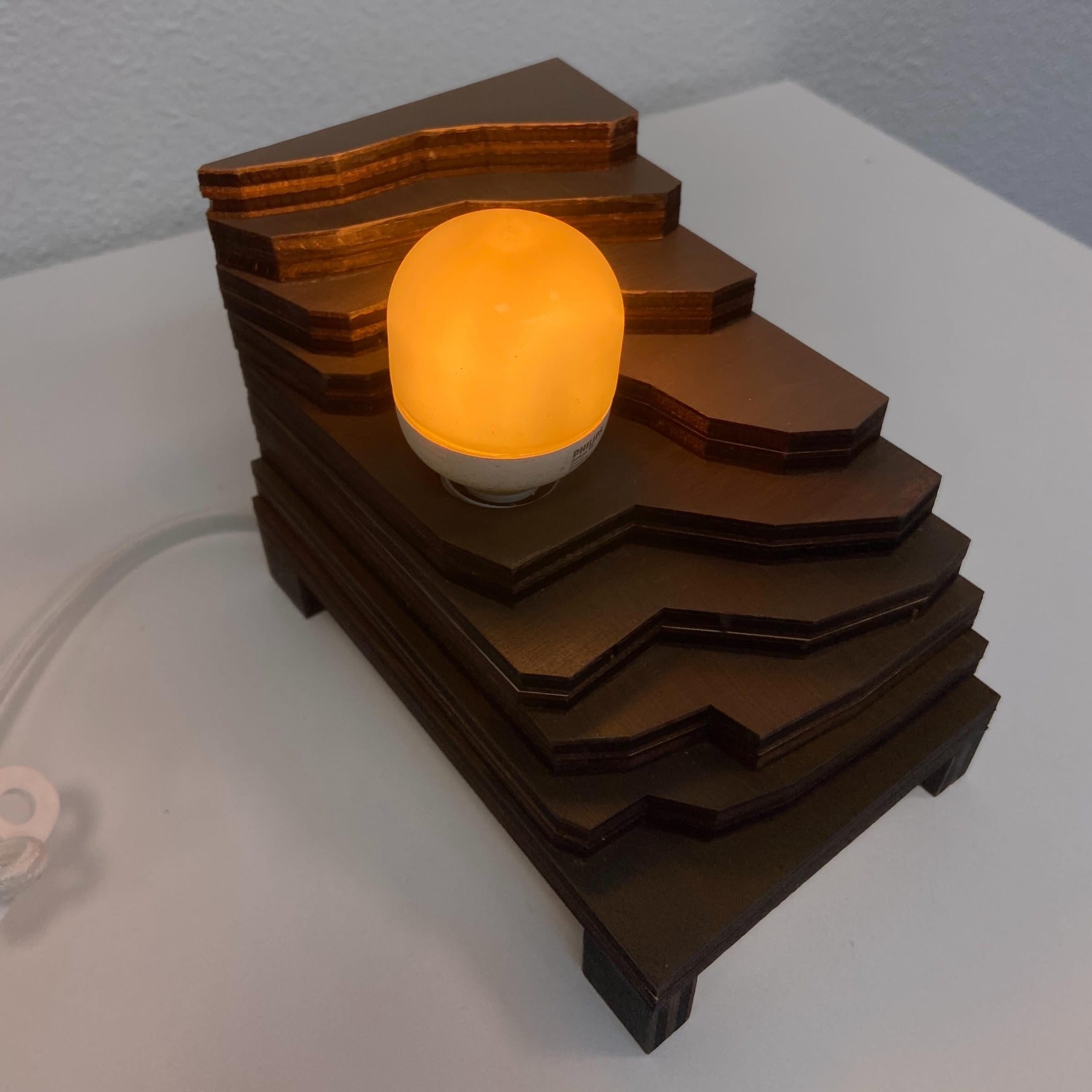 Lamp van gestapelde, getrapte houten platen met een oranje gloeiende bol