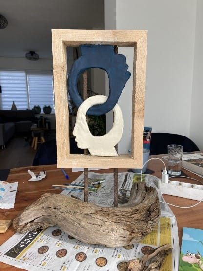 Houten lijst met een blauwe en een witte gekrulde vorm, gemonteerd op een stuk drijfhout
