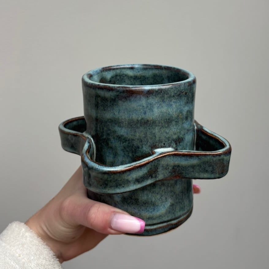 Hand die de blauwgroene beker met de golvende band vasthoudt