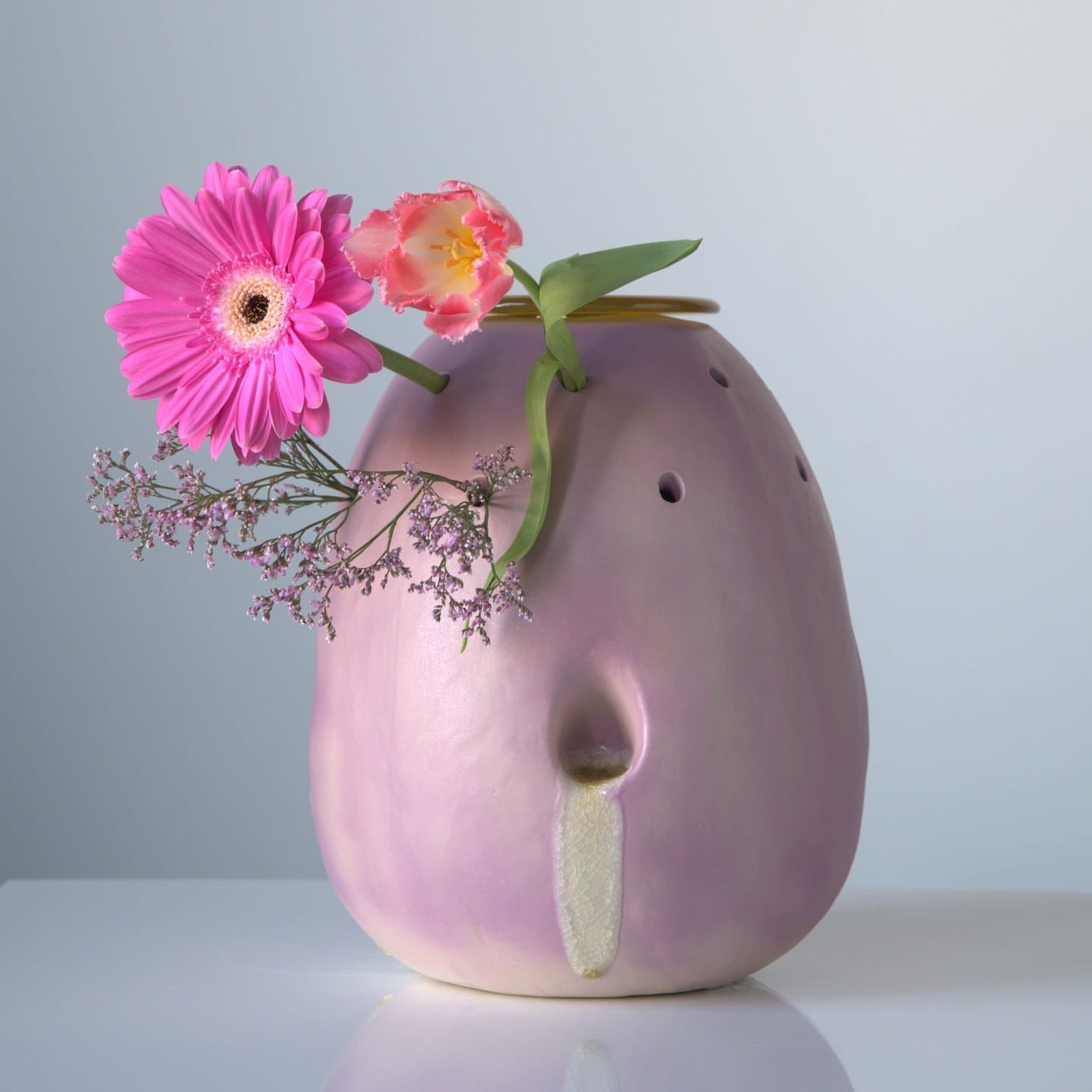 De lila vaas Bijziend met een roze gerbera, een tulp en lila bloempjes die uit de gaatjes in de wand steken