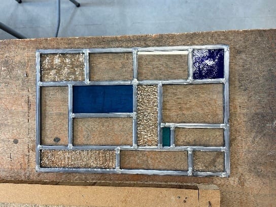 Glas-in-loodpaneel in aanbouw op een werkbank, met blauw en structuurglas