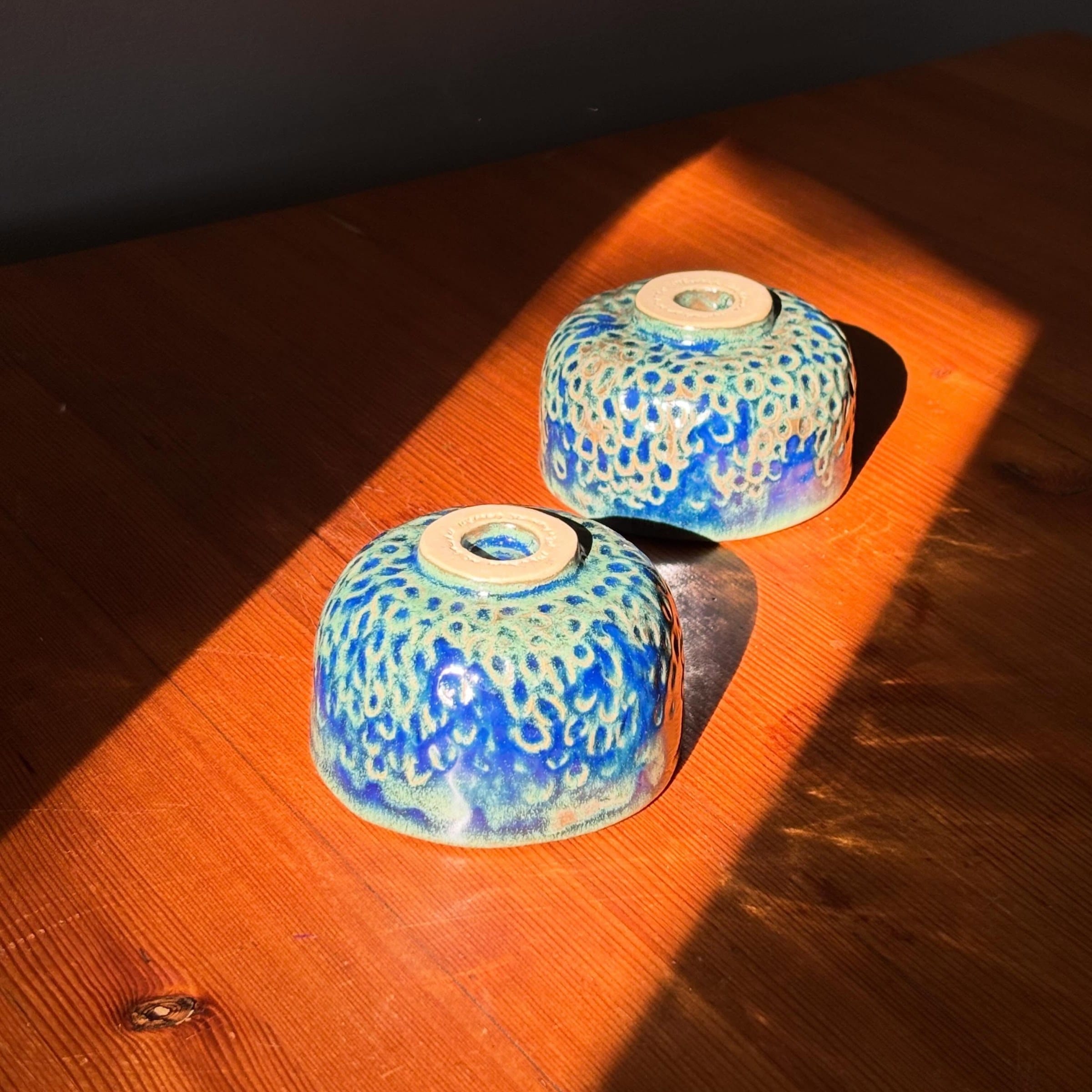 Twee blauwe kommetjes ondersteboven in het zonlicht, met de onverglaasde voet zichtbaar