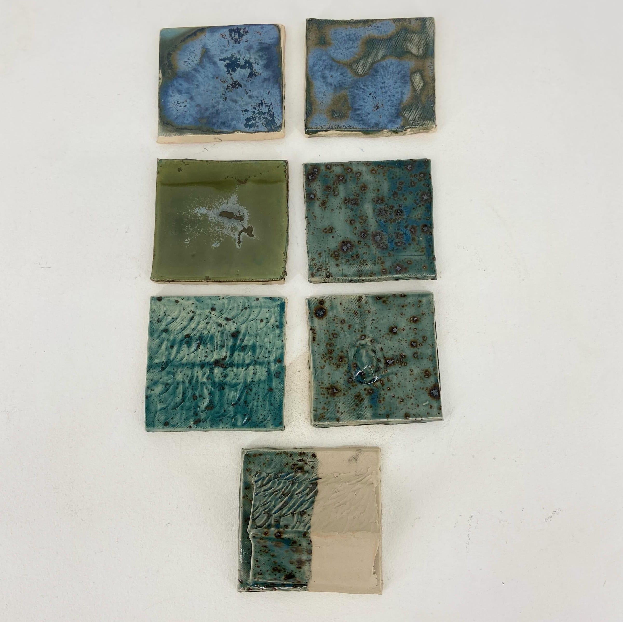 Glazuurtests in rijen, van gevlekt blauw tot glanzend olijfgroen