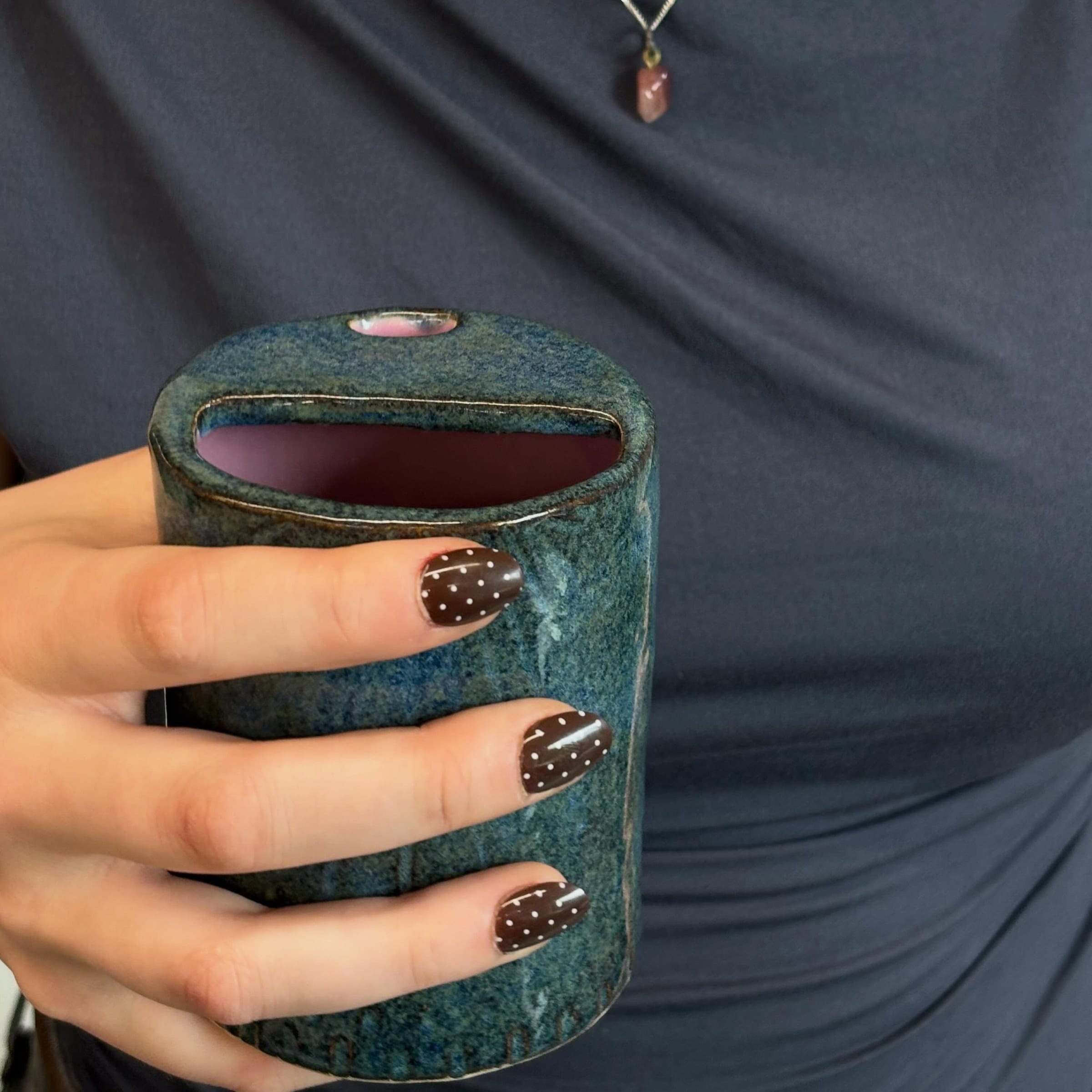 Hand met gestipte nagels die de blauwe cilindervaas vasthoudt