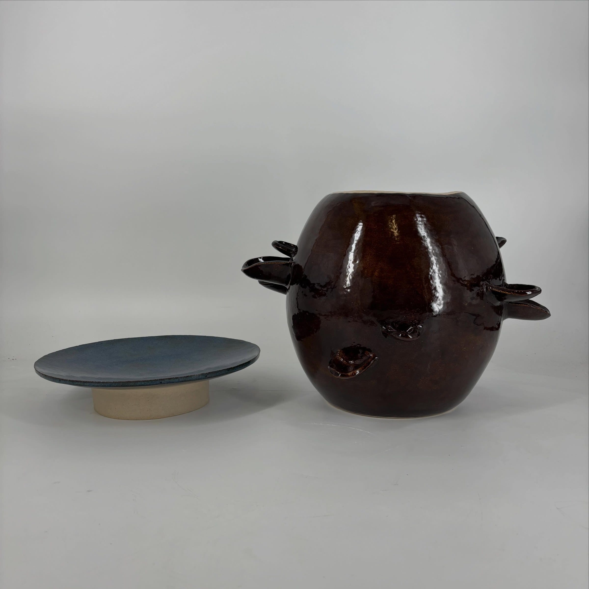 Blauw bord op een lage voet naast de donkerbruine pot