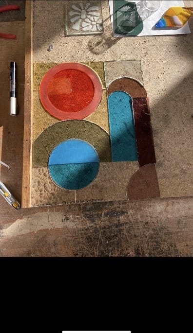 Glas-in-loodontwerp met cirkels en bogen in rood, blauw en goud op een werkbank