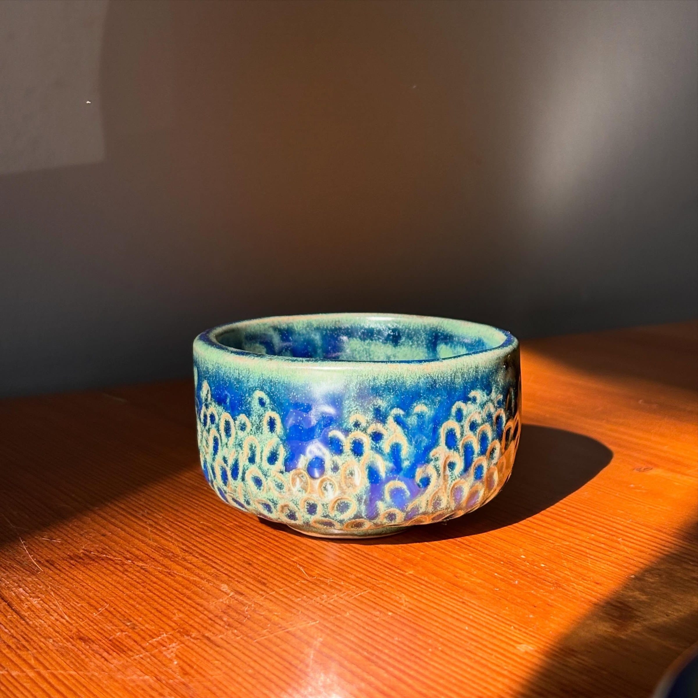 Blauw kommetje met reliëf en lichtgroen glazuur in schuin zonlicht