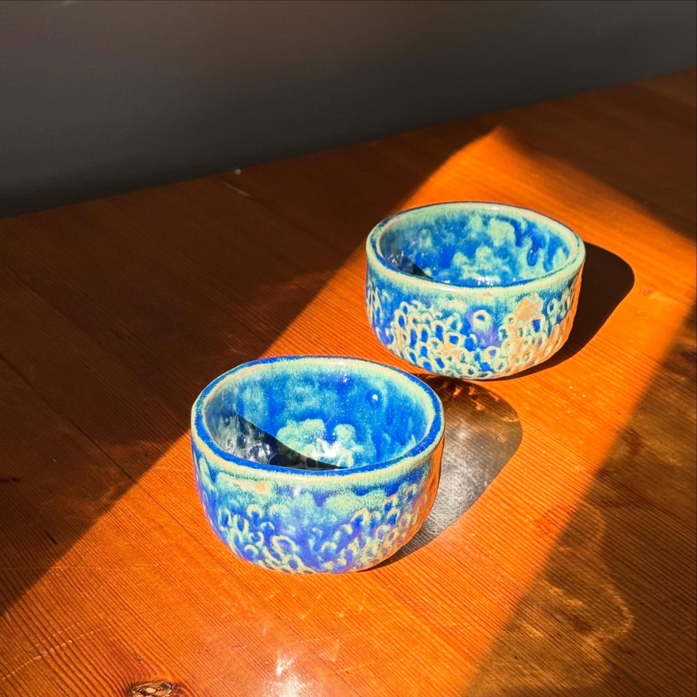 Twee blauwe kommetjes rechtop in het zonlicht op een houten tafel