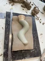 Een geboetseerde gebogen vorm op een plaat klei, voorbereid voor de mal