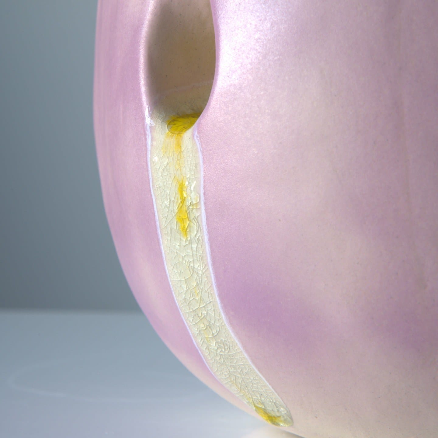 Detail van een gele, gecraqueleerde glazuurstreep die uit een opening in de lila wand loopt