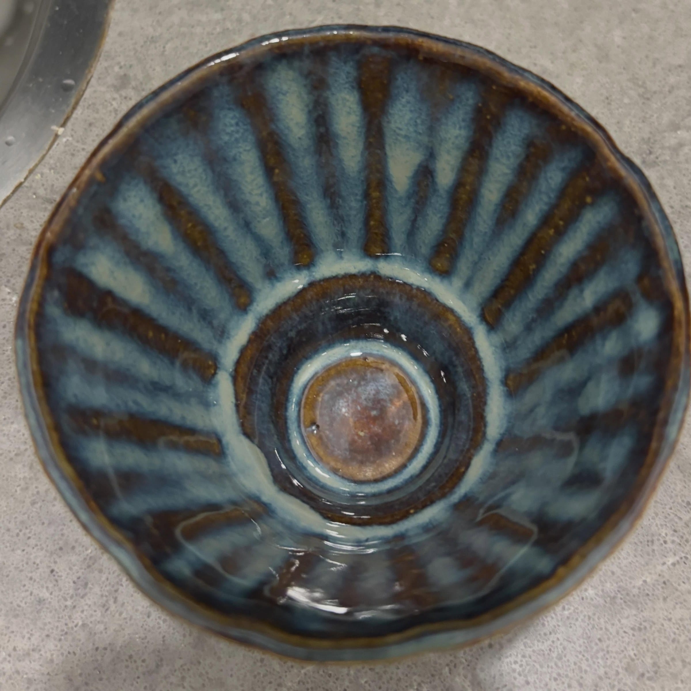 Binnenkant van een geribbelde kom van bovenaf, met stralen van blauw en bruin glazuur