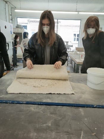 Een lap klei wordt uitgerold op een werktafel in de werkplaats van school