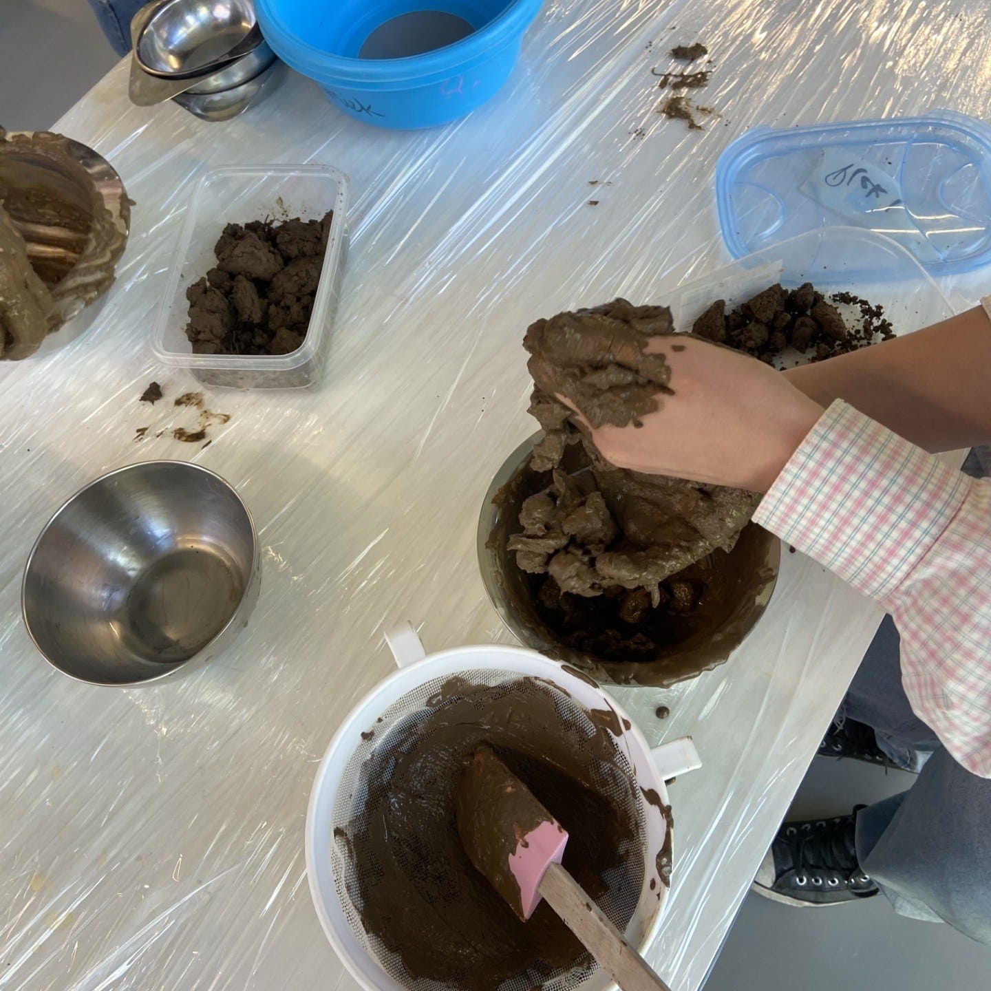 Handen die ruwe klei met water vermengen in kommen op een tafel met plastic
