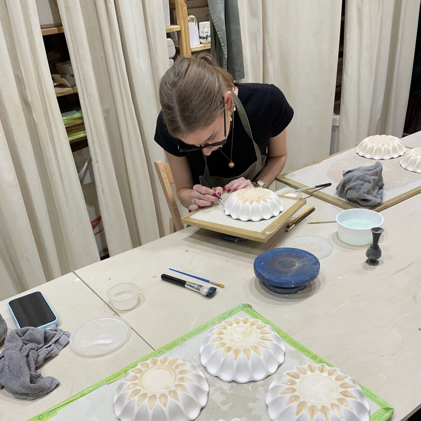 Aan een tafel in het atelier wordt een geribbelde vorm afgewerkt, met drie witte vormen op de voorgrond
