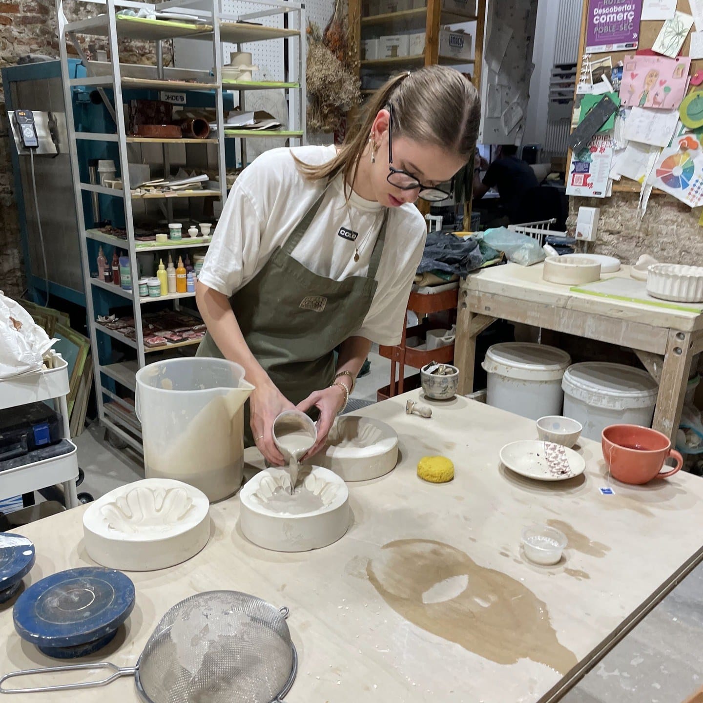 In het atelier aan de werktafel, bezig met een gipsmal en een kan gietklei